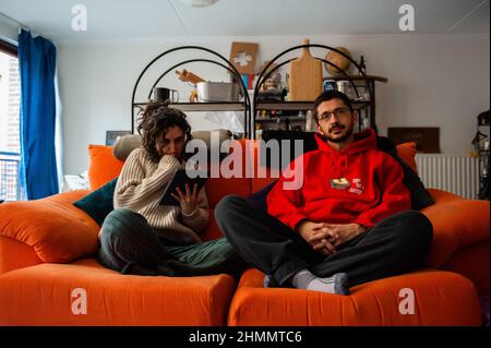 Nijmegen, Niederlande. 10th. Februar 2022. Ein Paar sitzt zu Hause auf der Couch, nachdem es die Heizung heruntergedreht und gemütliche Pullover getragen hat.der Warm Sweater Day wird jedes Jahr an einem Freitag im Februar vom Klimaatverbond Nederland (Climate Association Netherlands) organisiert. Das ist ein Zusammenschluss öffentlicher Organisationen mit Ambitionen im Bereich Nachhaltigkeit und Klimawandel. Es handelt sich um eine nationale Klimaschutzmaßnahme, bei der alle Teilnehmer versprechen, die Heizung in ihren Häusern, Büros, am Arbeitsplatz oder in ihren Klassenzimmern zu senken. Statt den Raum zu erhitzen, heizen sie Stockfoto