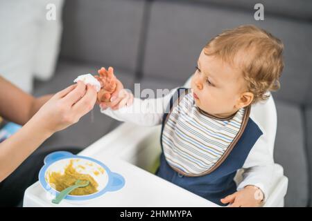 Niedliches Baby wurde schmutzig, während sie aß und Mutter putzt ihn. Stockfoto