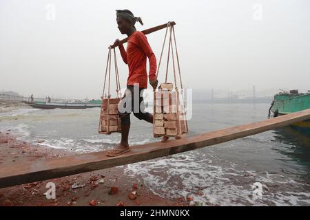 Dhaka, Bangladesch. 10th. Februar 2022. Arbeiter aus Bangladesch entladen Ziegelsteine aus einem Boot am Ufer des Flusses Buriganga, Dhaka, Bangladesch, 10. Februar 2022. Der Buriganga River ist einer der am stärksten verschmutzten und biologisch toten Flüsse der Welt. Foto von Suvra Kanti das/ABACAPRESS.COM Quelle: Abaca Press/Alamy Live News Stockfoto