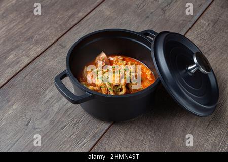 Stillleben von geschmorten Kutteln mit Chorizo in einer eisernen Kasserolle auf einem Holzbrett, typische Küche der Stadt Madrid. Traditionelle spanische Gastronomie Stockfoto