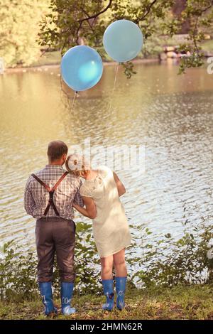 Junges Paar mit Ballons in den Händen an der Küste des Sees. Mann und Frau sind verliebt. Konzept für Postkarte oder Valentinstag. Zwei blaue Stockfoto