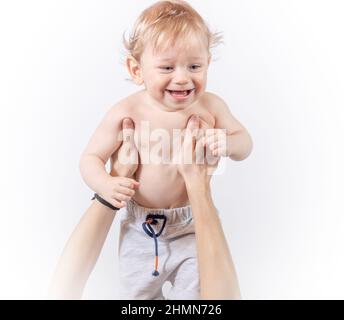 Ein kleines Kind lacht in den Armen einer Mutter, die ihn auf weißem Hintergrund hochhebt Stockfoto