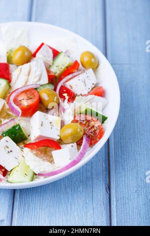 Griechischer Salat. Traditionelles griechisches Gericht. Gesundes vegetarisches Essen. Frisches Gemüse und Feta-Käse auf einem weißen Teller. Nahaufnahme, blauer Hintergrund. Stockfoto