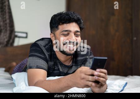 Glücklich lächelnder junger Mann beschäftigt mit Mobie Telefon in der Nacht auf dem Bett - Konzept der Verwendung von Dating-Anwendung, Social Media und Online-Chat Stockfoto