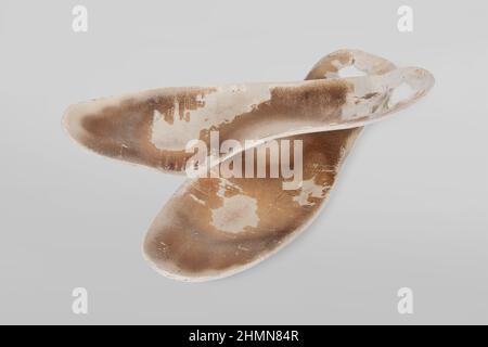 Zwei alte, schäbige orthopädische Einlagen isoliert auf grauem Hintergrund. Schmutzige Ledereinlagen. Verschlissene Sachen mit Löchern. Innensohle der Schuhe. Draufsicht Stockfoto