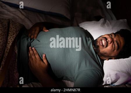 Junger Mann, der an Magenschmerzen oder Magenschmerzen leidet, während er nachts schläft - Konzept von Gesundheitsproblem, Lebensmittelvergiftung und ungesund Stockfoto