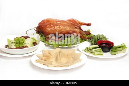 Peking-Ente, chinesische gebratene knusprige Ente, serviert mit Hoisin-Sauce, Pfannkuchen und grünem Gemüse auf weißem Hintergrund. Stockfoto