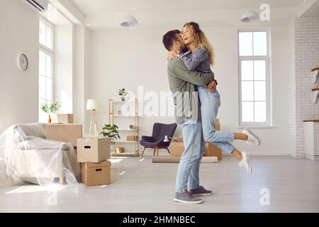Glückliches Ehepaar hat Spaß, umarmt und freut sich aufrichtig über den Umzug in ein neues Zuhause. Stockfoto