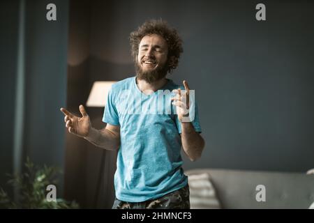 Entspannter junger Mann mit zerzausten Tellern, der sich nach langen Arbeitszeiten während der Quarantäne zu Hause im Tanz ausdehnt. Junge gutaussehende Freiberuflerin zu Hause genießen Freizeit. Stockfoto