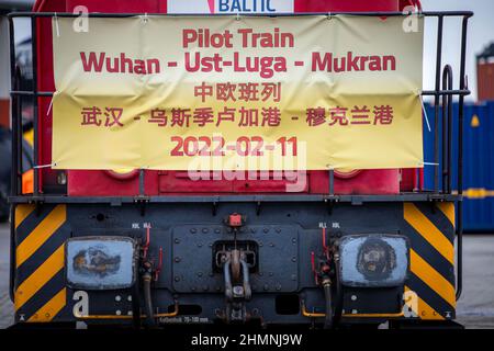 Mukran, Deutschland. 11th. Februar 2022. An einer Lokomotive hängt ein Transparent mit der Aufschrift „Fliegerzug Wuhan-USt-Luga-Mukran“, der die ersten Container einer neuen „Seidenstraße“ zwischen China und Deutschland durch den Hafen von Mukran zieht. Die Container aus dem chinesischen Wuhan decken einen Teil der Strecke auf dem Wasser ab und werden auf der Insel Rügen wieder auf Schienenfahrzeuge verladen. Quelle: Jens Büttner/dpa-Zentralbild/dpa/Alamy Live News Stockfoto