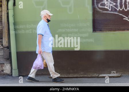 RIGA, LETTLAND. 3rd. Juli 2021. Selektiver Fokus auf Foto. Ein Mann mit Gesichtsmaske geht mit einer Plastiktüte auf die Straße. Stockfoto