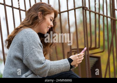 Junge Rotschopf-Frau, die ihr Smartphone im Park ansieht Stockfoto