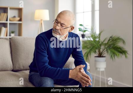 Älterer Mann in einer Brille sitzt zu Hause auf dem Sofa, blickt auf etwas und denkt nach Stockfoto