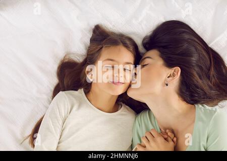 Die glückliche Mutter küsst ihre Tochter auf die Wange, als sie sie am Morgen aufweckt Stockfoto