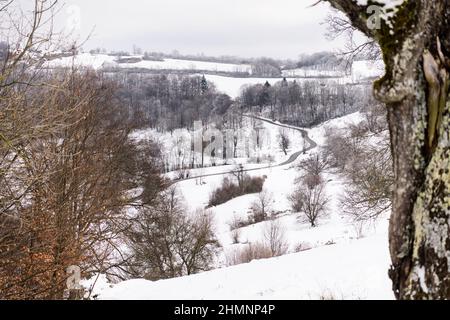 Kurvenreiche Straße durch verschneite Landschaft im ländlichen Raum in Deutschland im Winter Stockfoto