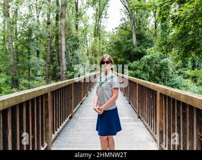 Porträt einer 30-jährigen weißen Frau in einem Sommerkleid, die auf einer hölzernen Fußgängerbrücke steht Stockfoto