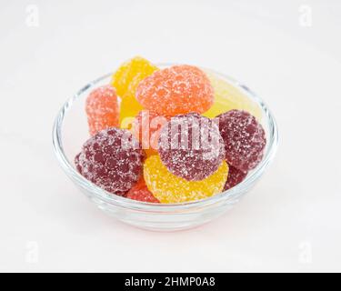 Mehrfarbige Marmelade aus Saft in Form von Beeren und Früchten in einer Glastasse auf weißem Grund Stockfoto