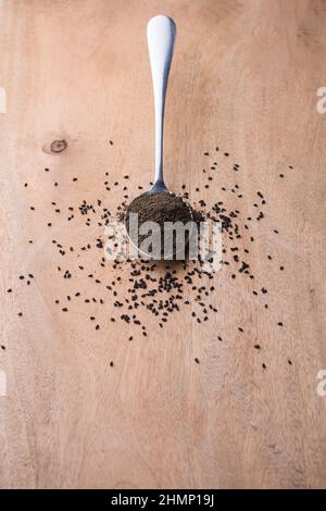 Gepulverte und geröstete schwarze Samen, auch als schwarzer Kümmel oder Kümmel oder Kalonji bekannt, in einem Löffel, mit verstreuten Samen auf einer Tischplatte, geringe Tiefe von f Stockfoto