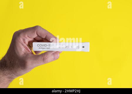 Männliche Hand mit negativem Covid-19- und omicron-Antigentest auf gelbem Hintergrund Stockfoto
