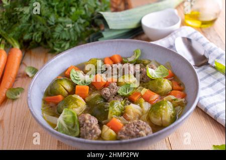 Kohlsuppe mit Gemüse, braunem Reis und Hackfleisch. Glutenfreies Abendessen oder Mittagessen. Serviert auf einem Teller mit Löffel auf dem Küchentisch Stockfoto