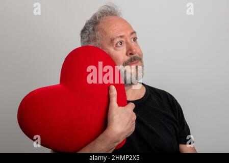 Schöner grauhaariger und bärtiger Mann mittleren Alters mit einem roten Herzen und isoliertem grauen Hintergrund. Valentinstag-Konzept Stockfoto