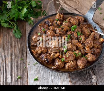 Rustikale Pfanne mit Fleischbällchen in einer köstlichen braunen Pilzsauce. Serviert in einer gusseisernen Pfanne isoliert auf einem Holztisch mit Platz zum Kopieren Stockfoto