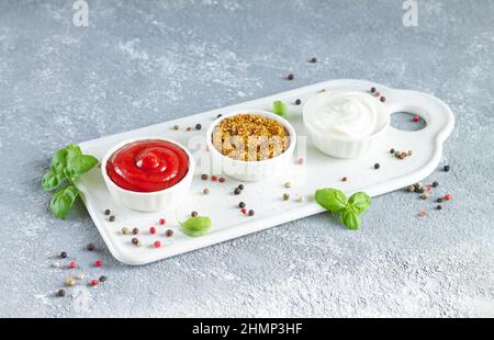 Set mit beliebten Saucen: Ketchup, dijon-Senf und Mayonnaise in kleinen weißen Schalen auf Keramikschale Stockfoto