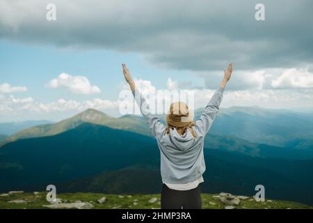 Schöne weibliche Wanderer erheben sich Hand auf den Berg und Sonnenuntergang Himmel Hintergrund. Reise-, Lifestyle- und Fernweh-Konzept. Rückansicht Stockfoto