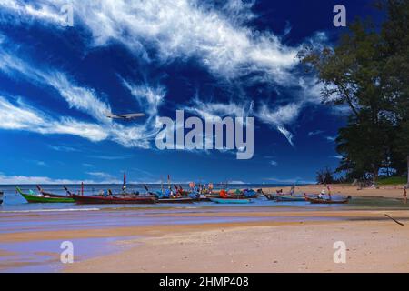 Ankunft in Phuket - Blick über tropischen Sandstrand und Longtail-Boote auf Landeplatz gegen tiefblauen Sommerhimmel - Nai Yang in der Nähe des Flughafens, Thailand Stockfoto