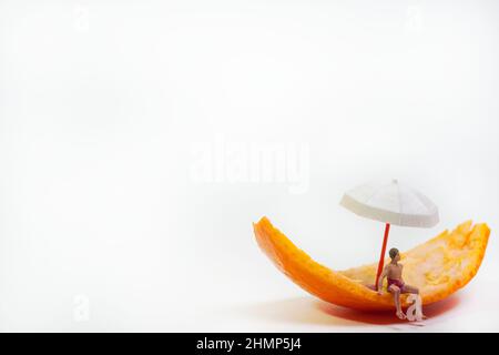 Ein Mann in Badehosen sitzt auf einer Mandarinenschale unter einem Regenschirm Stockfoto