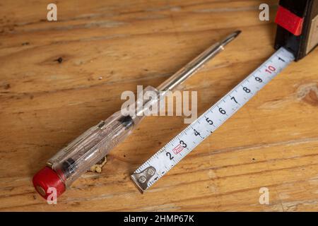 Auf einem Holztisch liegen alte elektrische Spannungsprüfer und weißes Messband, Werkzeuge für Heimwerker Stockfoto
