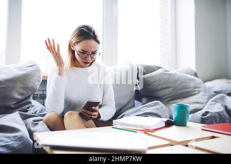 Verwirrte Frau, die im gemütlichen Büro ein Mobiltelefon anwählt Stockfoto