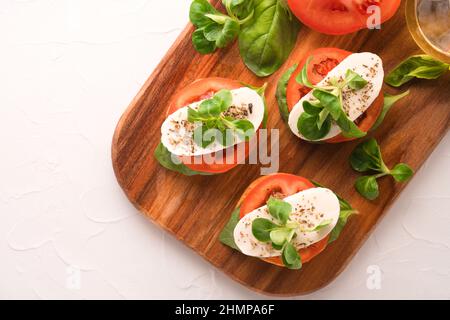 Blick von oben auf den klassischen italienischen Caprese-Salat mit geschnittenen Tomaten, Mozzarella und Basilikum auf Bruschettas auf einem hölzernen Servierbrett auf weißem Tischhintergrund. Stockfoto