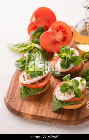 Vertikales Bild des klassischen italienischen Caprese-Salats mit geschnittenen Tomaten, Mozzarella und Basilikum auf Bruschettas auf Holzplatte auf weißem Tischhinterteil Stockfoto