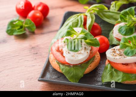 Nahaufnahme der traditionellen italienischen Vorspeise - Caprese-Salat mit geschnittenen Tomaten, Mozzarella, Basilikum und garniert mit Maissalat auf Bruschettas auf schwarzem Pl Stockfoto