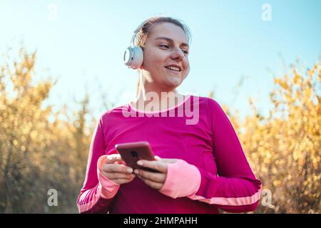 Fitnessläufer, die im Freien laufen und Musik über Kopfhörer auf dem Smartphone hören. Weibliche Fitness Mädchen Joggen Herbst Natur Landschaft draußen. Stockfoto