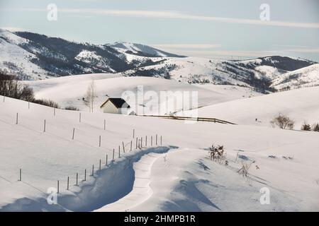 Winter idyllisch mit kleiner Hütte auf Bergort Zlatibor, Serbien, Europa und Straße in ländlicher Landschaft. Tornik Ski-Zentrum in der Ferne Stockfoto