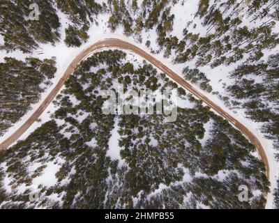 Kurvenreiche Straße In Der Winterlandschaft. Luftaufnahme von Drohne der Straße zwischen Bäumen im verschneiten Wald. Stockfoto