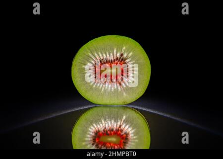 Scheibe einer Kiwi isoliert in dunkelschwarzem Hintergrund mit Reflexion, perfekte Symmetrie Stockfoto