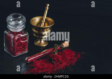 Rohes Bio-Safrangewürz aus rotem getrocknetem Safran auf Holzhintergrund in Vintage-Messingmörtel aus Metall mit Stößel, Glasgefäß und Rohr Stockfoto