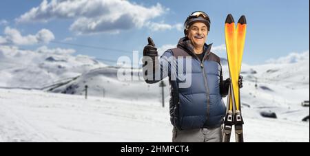 Reifer Mann, der ein Paar Skier hält und Daumen hoch auf einem Berg zeigt Stockfoto