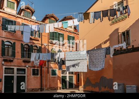 Wäsche hängt aus der typischen venezianischen Fassade, Italien. Enge Straße mit bunten Gebäuden und Kleidung trocken am Seil, Venedig. Saubere Kleidung trocknen im Freien Stockfoto