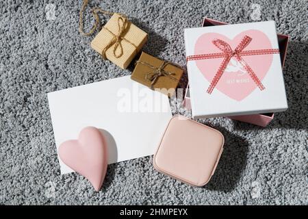 Grußkarte zum Valentinstag. Umschläge, eingewickelte Schachteln, Keramik rosa Herz auf einem grauen flauschigen Teppich Hintergrund. Speicherplatz kopieren. Für Text platzieren Stockfoto