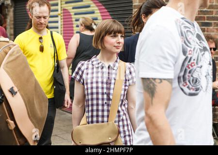 London, Großbritannien - am 17. Juli 2020 spaziert Ein kurzhaariges Mädchen in einem karierten Kleid mit einer Ledersatteltasche an einem Sonntagnachmittag entlang des Brick La durch die Menge Stockfoto