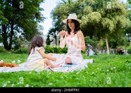 Junge Mama bläst Blasen für kleine Tochter im Park Stockfoto