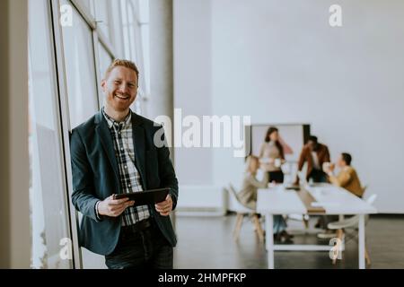 Junger, gutaussehender Geschäftsmann, der mit einem digitalen Tablet vor seinem Team im Büro steht Stockfoto