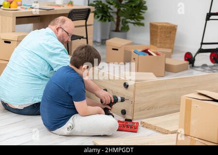 Ein Vater zeigt seinem Sohn, wie er einen Akkuschrauber hält. Stockfoto