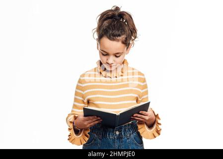 Junges Mädchen, das ein Buch liest, während es auf einem isolierten weißen Hintergrund steht. Stockfoto