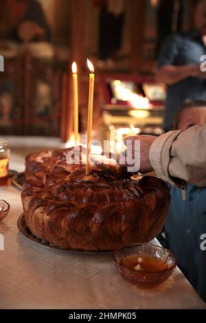 Nahaufnahme einer älteren Frau, die bei einer Taufe in einer Kirche einen Laib Brot schneidet Stockfoto