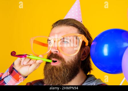 Bärtiger Mann mit Geburtstagskappe und Partyhorn. Mann in Papierkegel Hut und große Gläser mit Noisemaker. Stockfoto